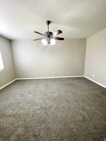 Unfurnished room with dark carpet, a ceiling fan, and a textured ceiling