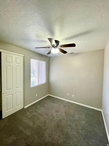 Unfurnished bedroom with dark carpet, a textured ceiling, a closet, and a ceiling fan