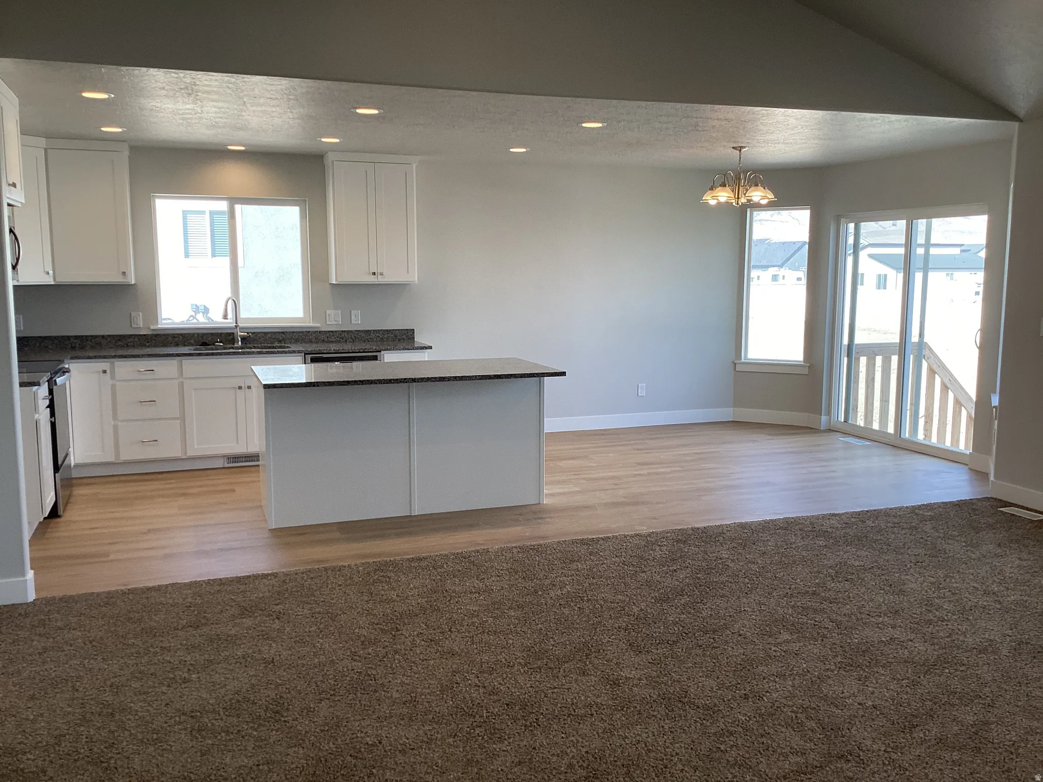 Kitchen with a center island, white cabinets, electric range, a chandelier, and light carpet
