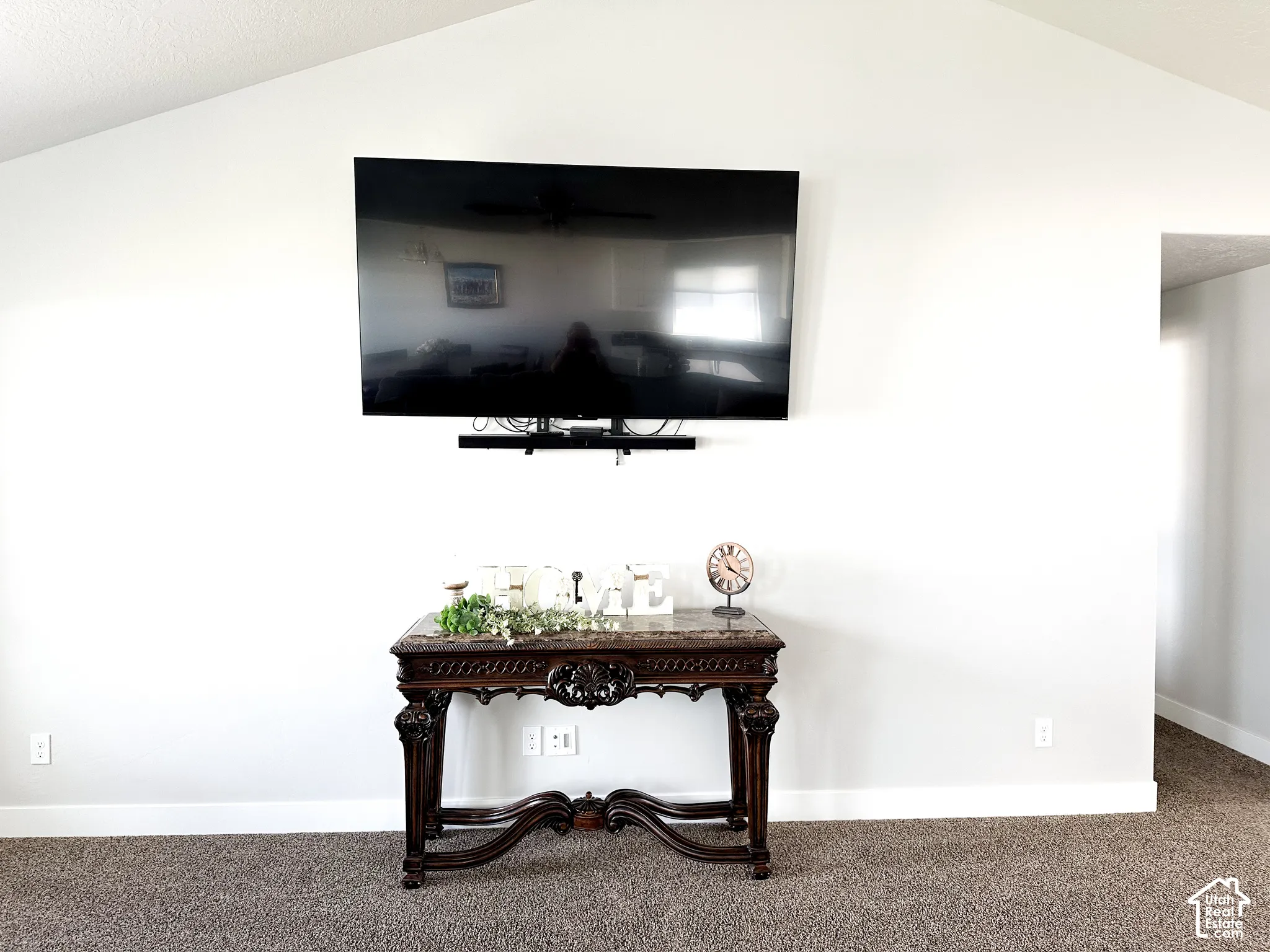 Vaulted ceiling with textured finish, wall-mounted television, and carpet flooring