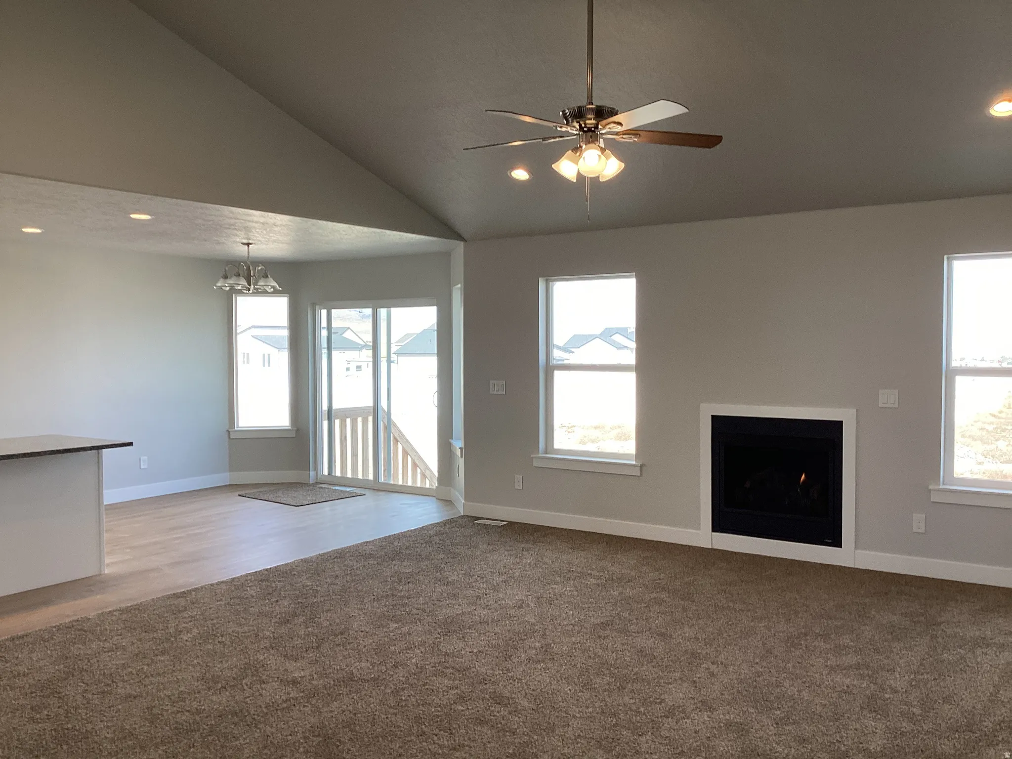 Unfurnished living room with a fireplace, light carpet, a ceiling fan, a chandelier, and lofted ceiling