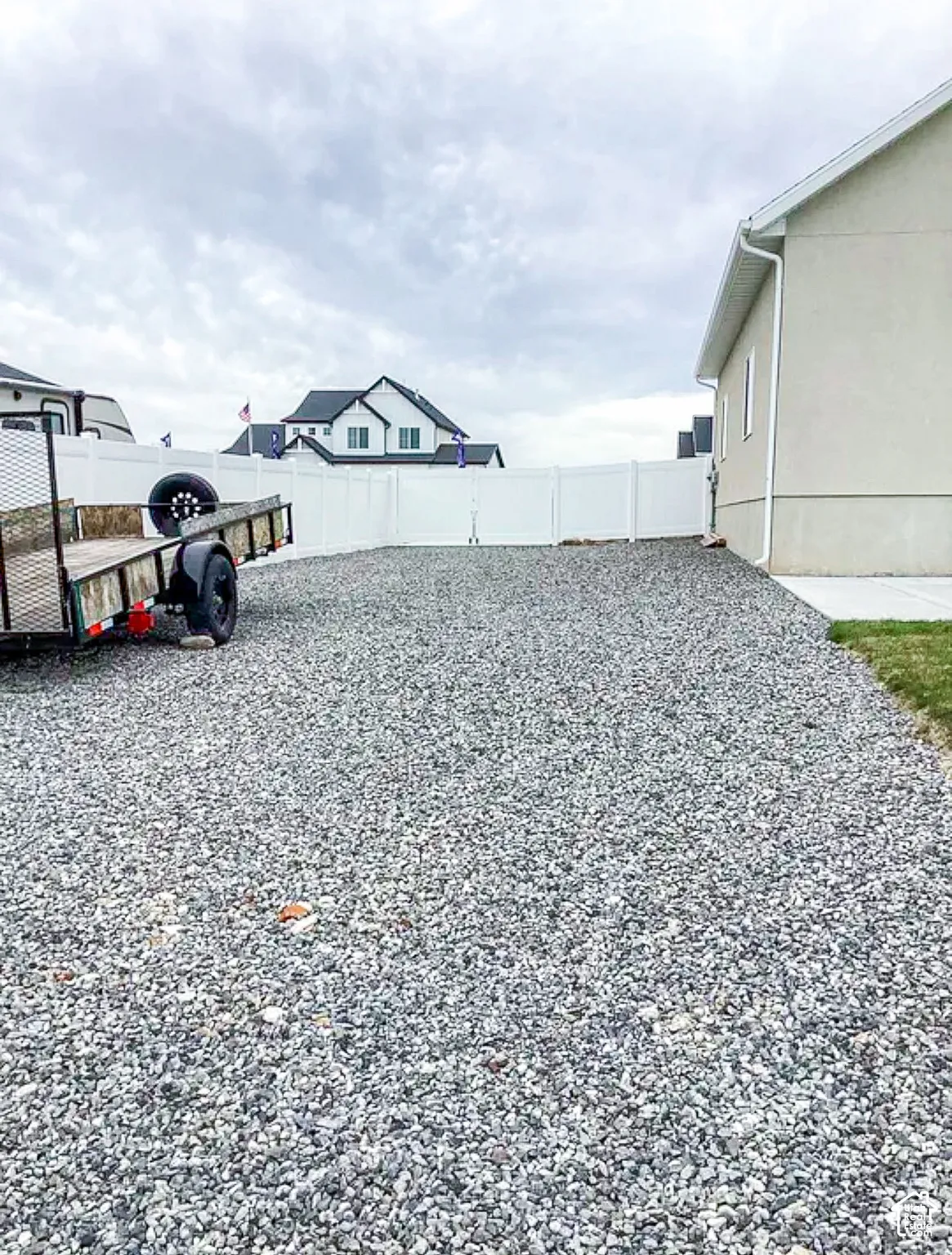 Expansive gravel area with white vinyl fencing and a stucco exterior