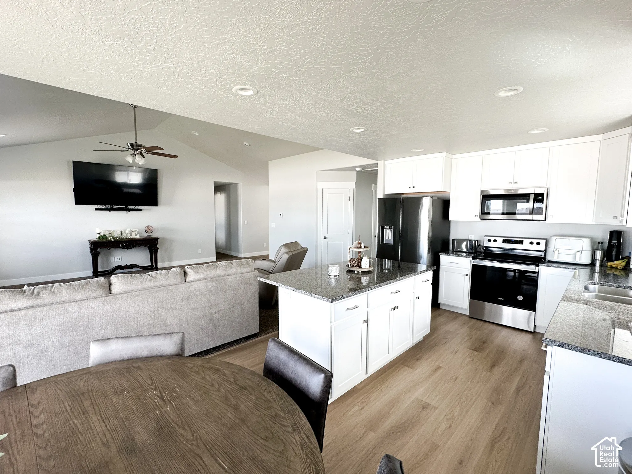 Kitchen featuring white cabinetry, stainless steel appliances, granite countertops, and wood-finish flooring