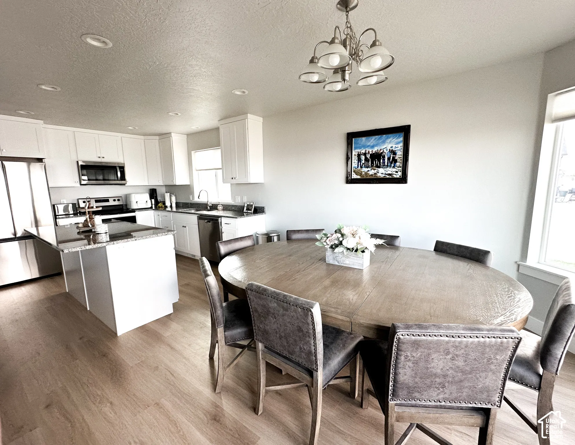 Kitchen and dining area featuring wood-finish flooring, white cabinetry, stainless steel appliances, and a kitchen island with a stone countertop