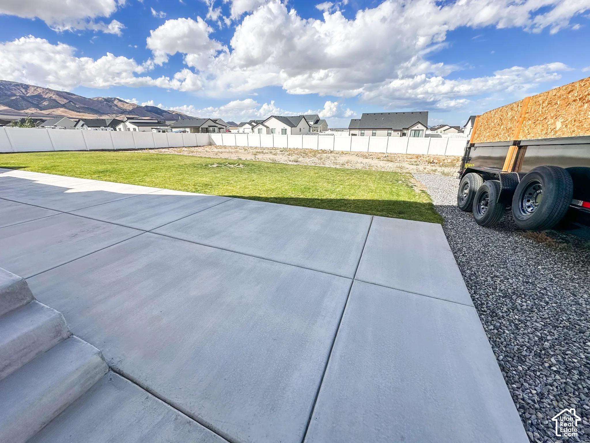 Expansive concrete patio with integrated steps, leading to a lawn area and a gravel path