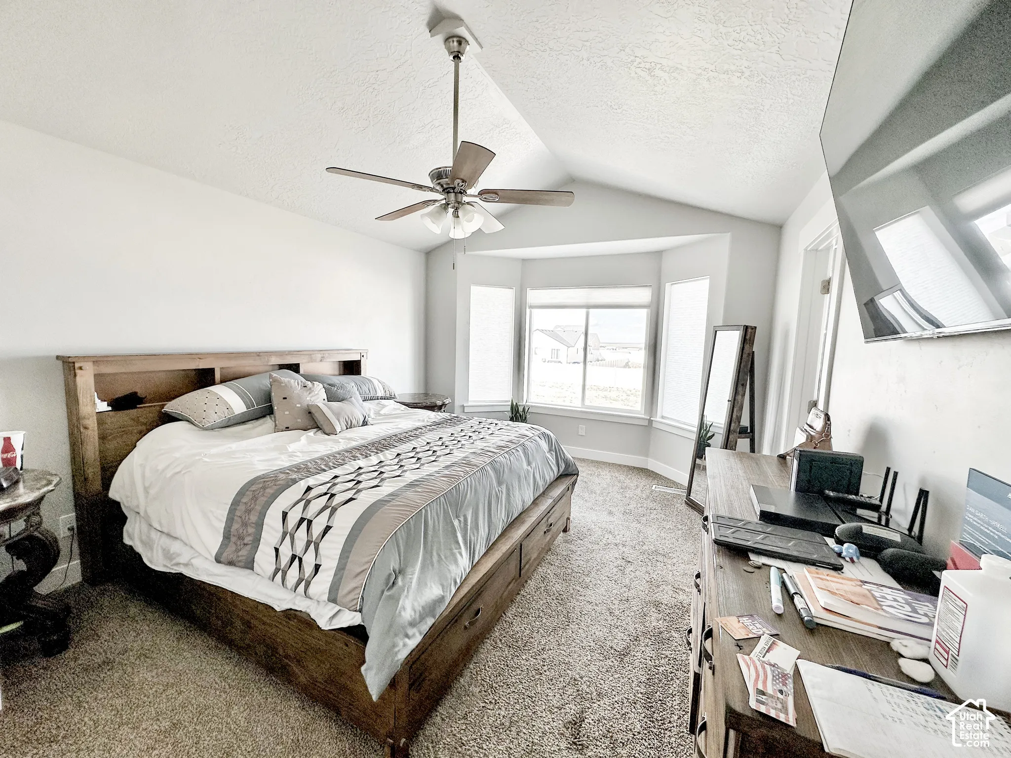 Vaulted ceiling with ceiling fan, bay windows, mounted television, and carpet flooring