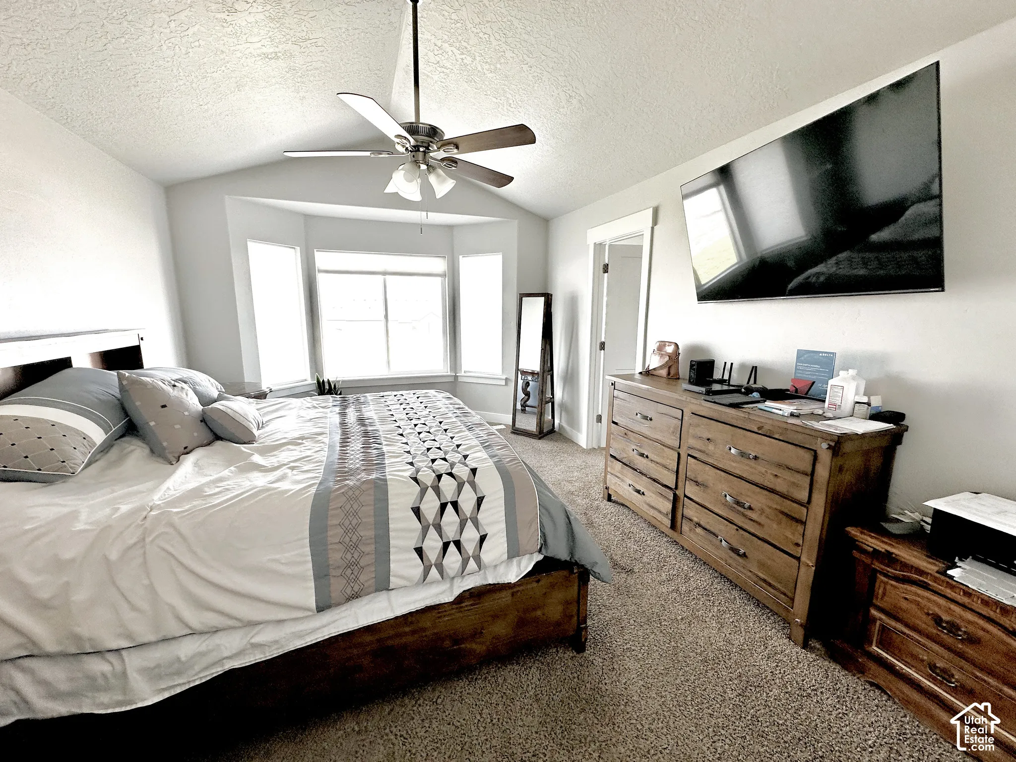 Carpeted room featuring a bay window, ceiling fan, and wall-mounted television