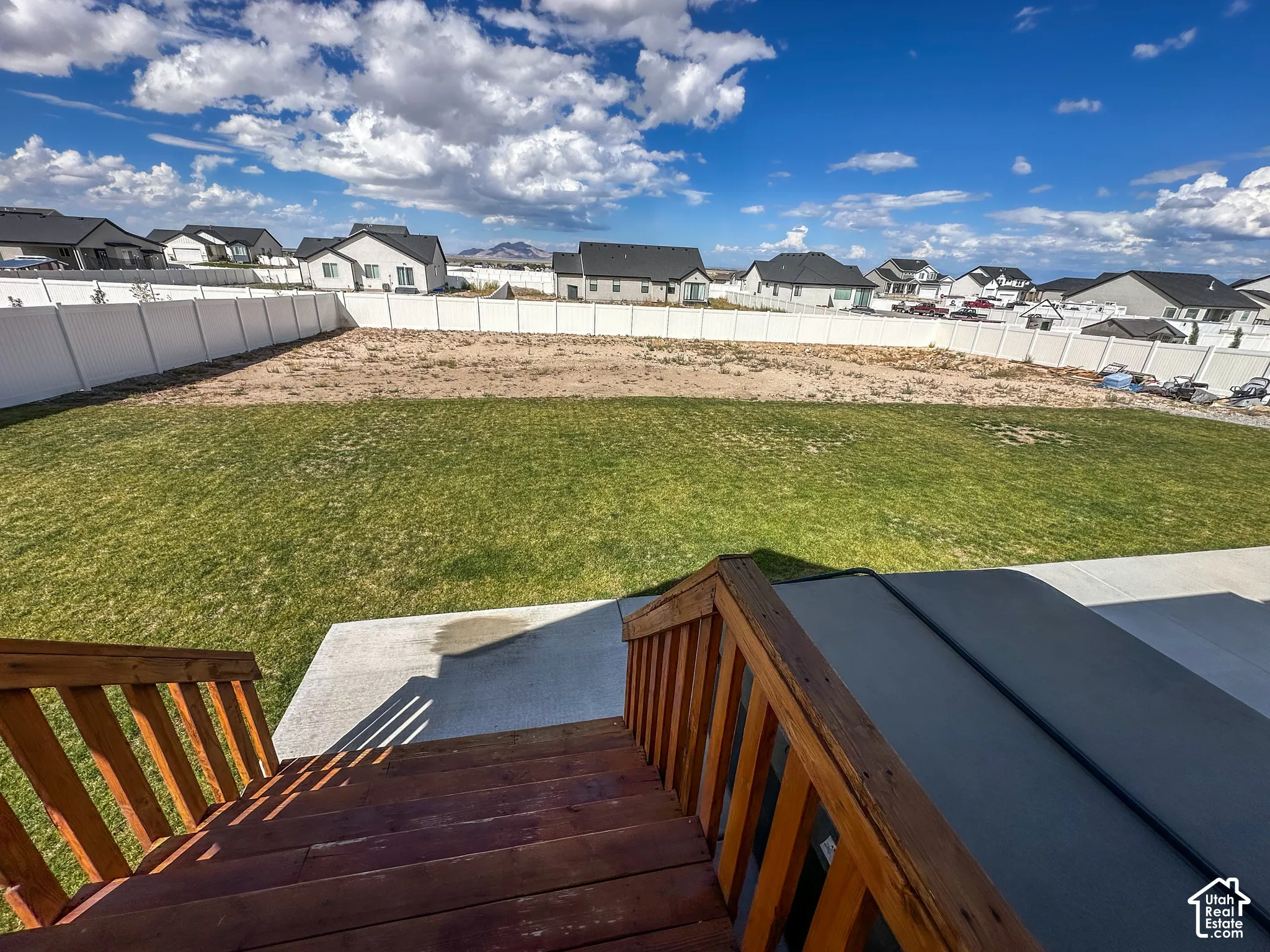 Expansive backyard featuring a partial manicured lawn, a large unlandscaped area, and a white privacy fence