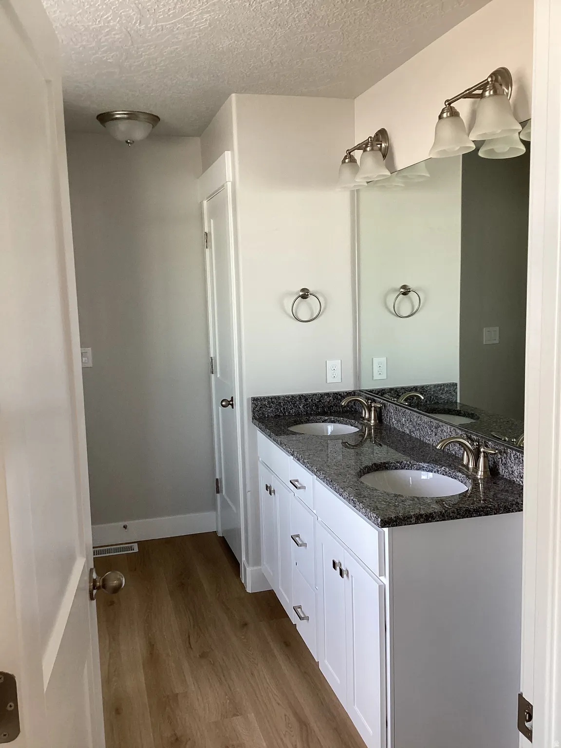 Bathroom with double vanity, a textured ceiling, and light wood-type flooring