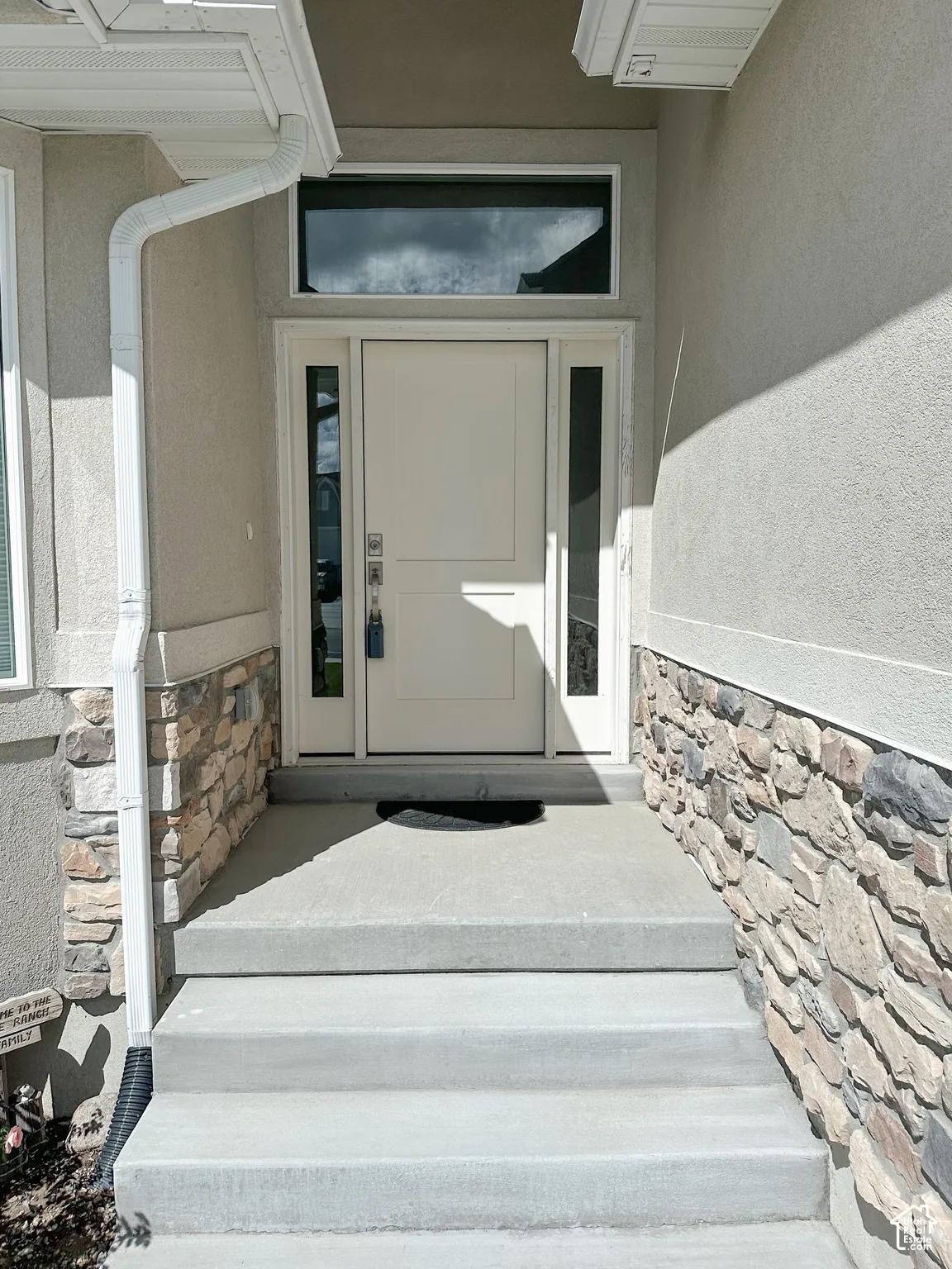 Inviting entry featuring a solid paneled door with glass side lites, a transom window, and stone veneer accents
