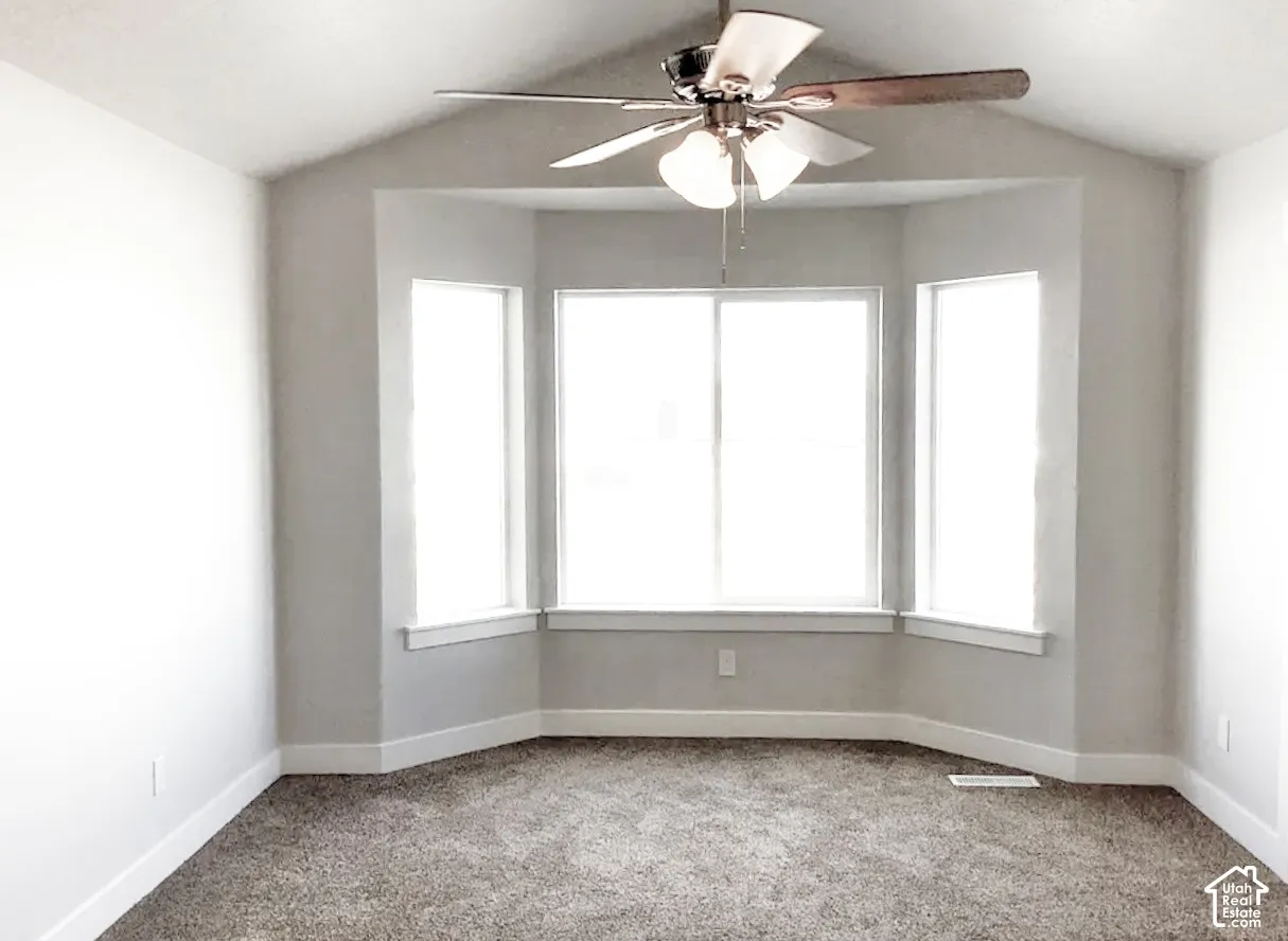 Vaulted ceiling, ceiling fan with light fixture, bay window, carpet flooring, and white trim