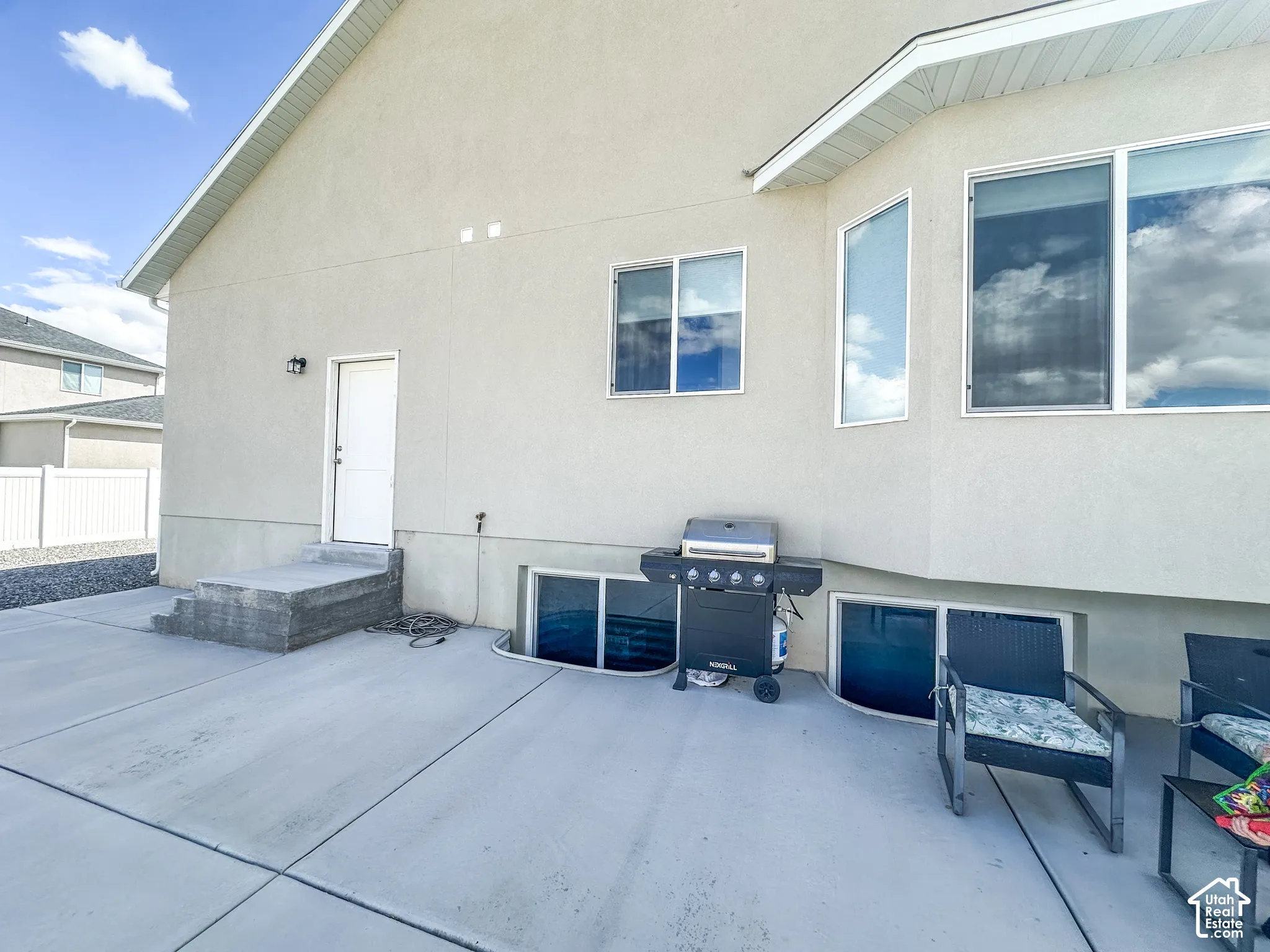 Concrete patio with a stucco exterior, multiple windows, and a white entry door