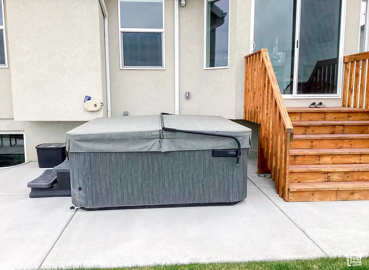 Concrete patio featuring a hot tub with cover, wood stairs, and exterior sliding glass door