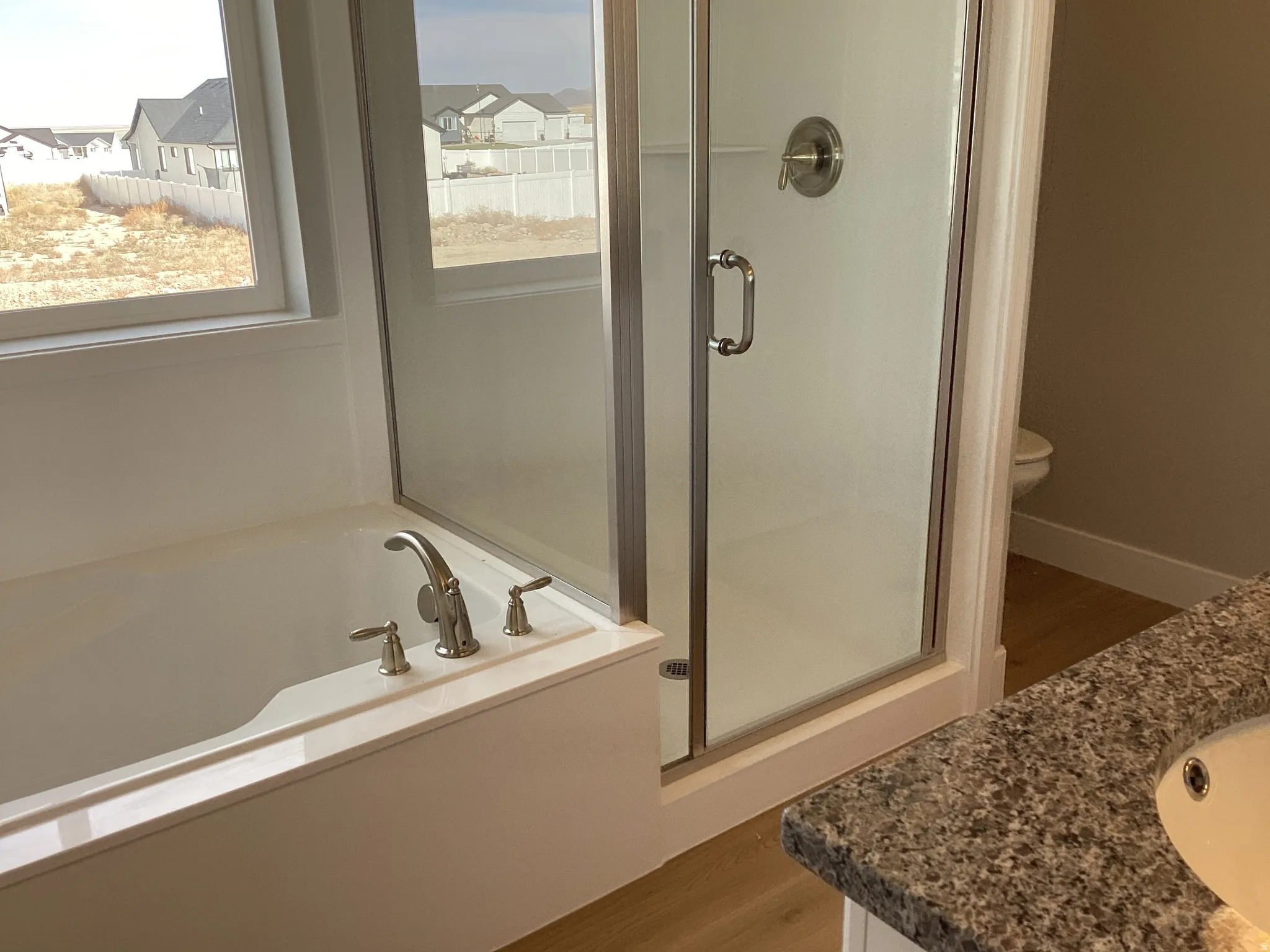 Bathroom featuring a garden tub, vanity, a shower stall, wood finished floors, and a residential view
