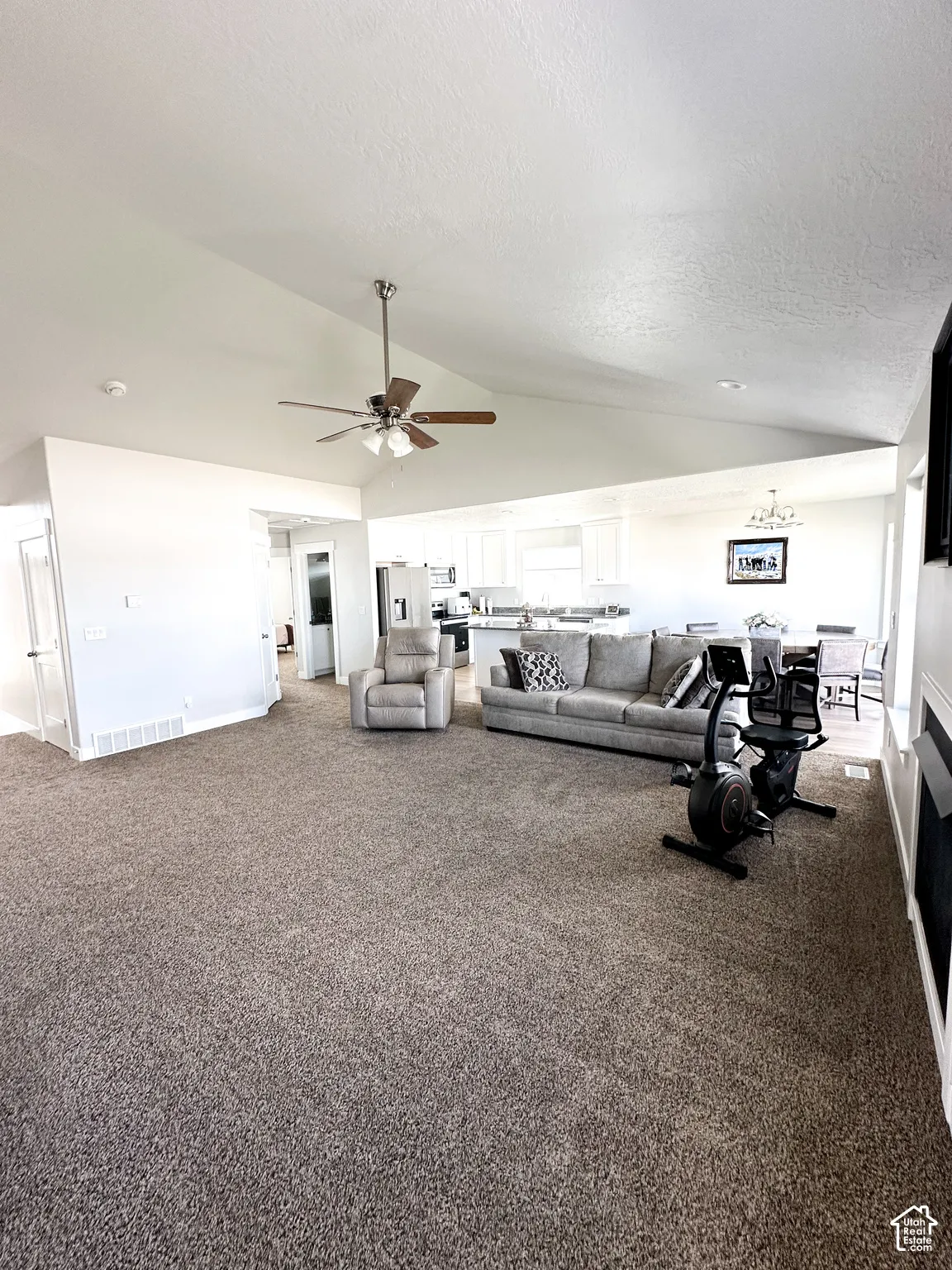 Vaulted ceiling, ceiling fan with light fixture, neutral wall paint, carpeted flooring, and built-in fireplace