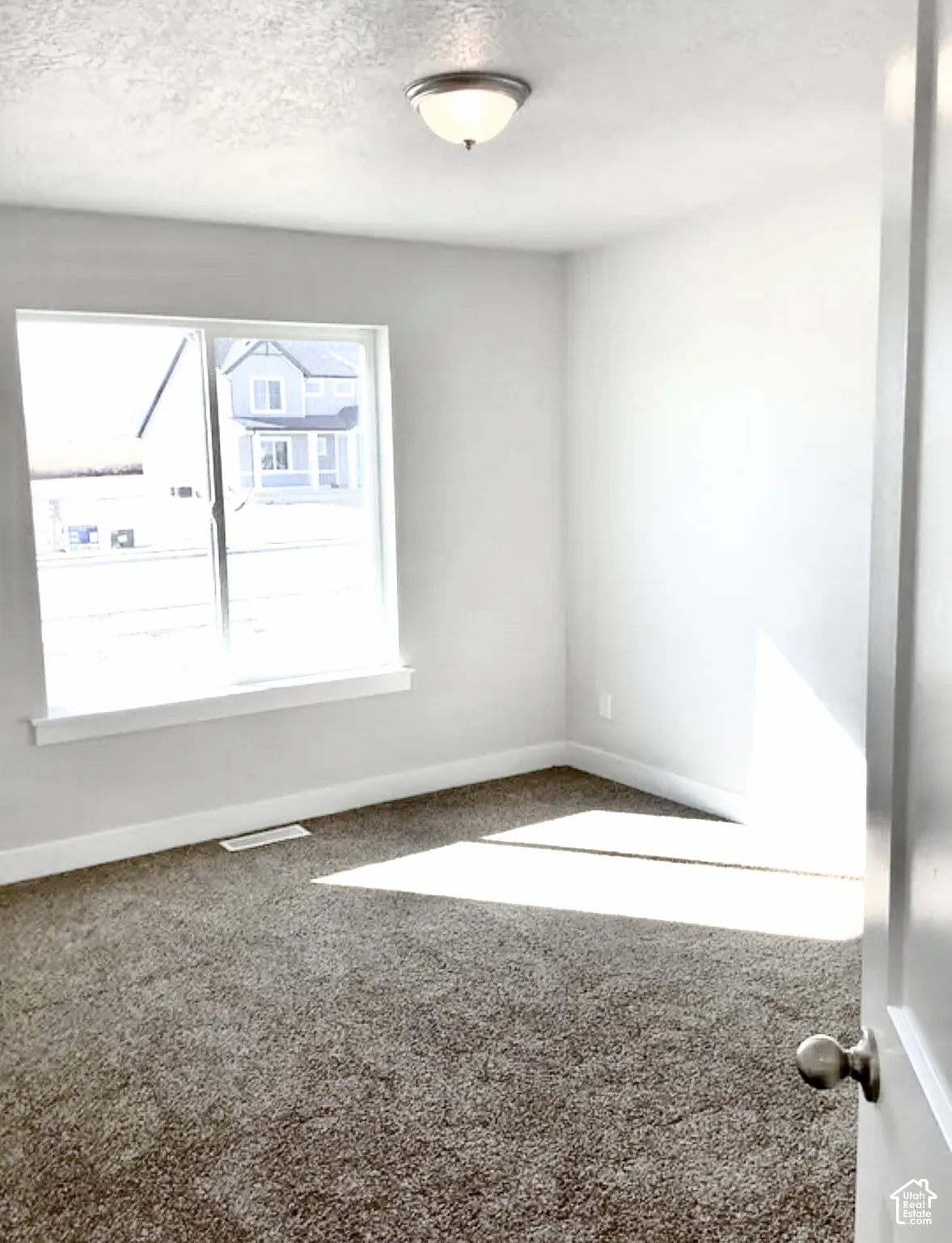 Neutral wall finishes, light-toned carpeting, flush-mount ceiling fixture, and a window with white trim