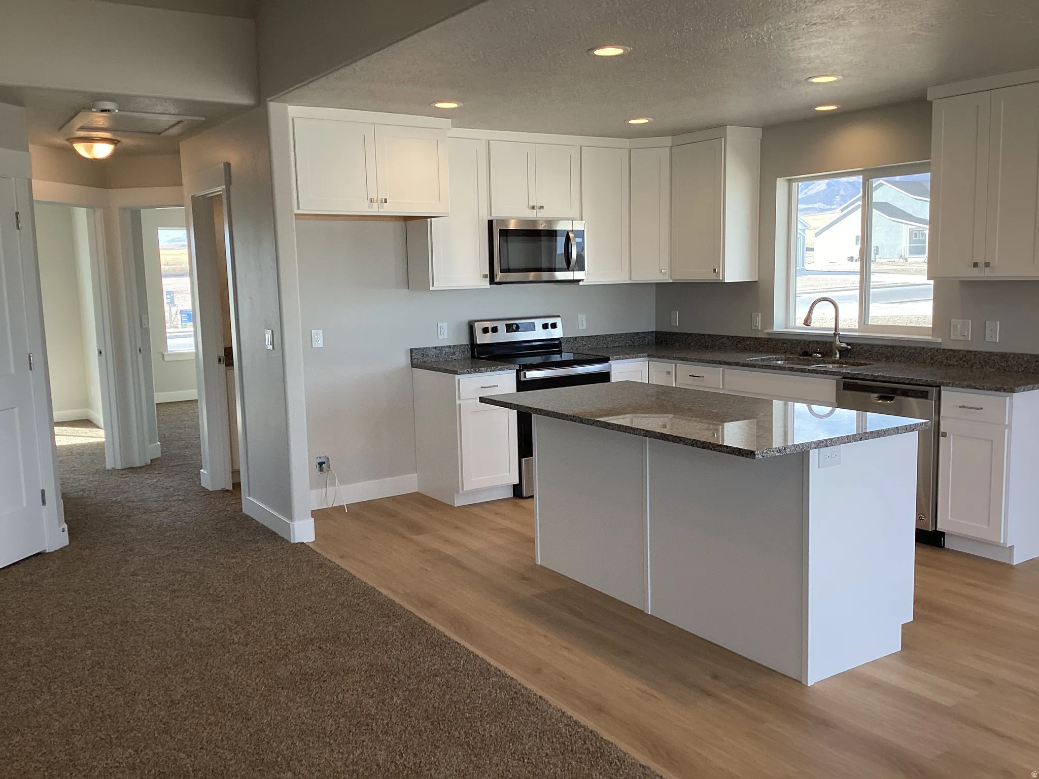 Kitchen with dark stone counters, stainless steel appliances, white cabinetry, recessed lighting, and light wood-type flooring