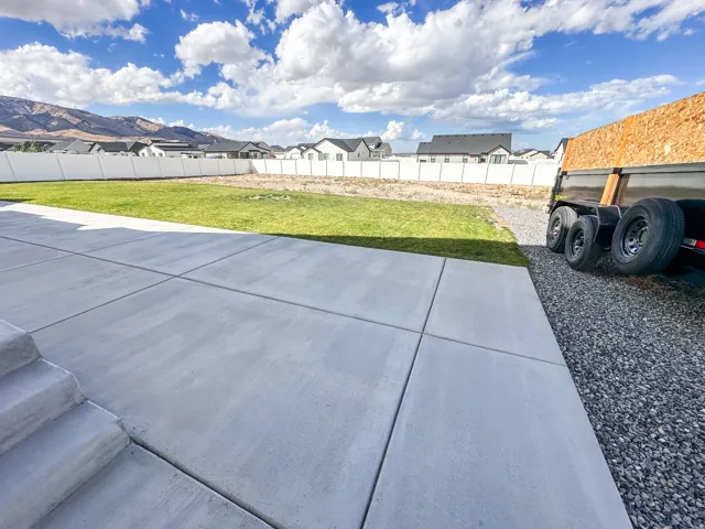 Expansive concrete patio with integrated steps, leading to a lawn area and a gravel path