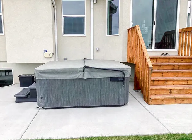Concrete patio featuring a hot tub with cover, wood stairs, and exterior sliding glass door