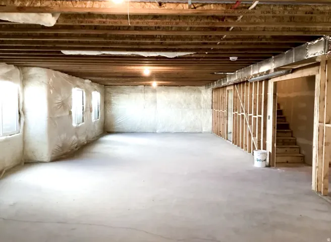 Unfinished lower level featuring exposed wood joists, concrete flooring, multiple windows, and partial wood framing