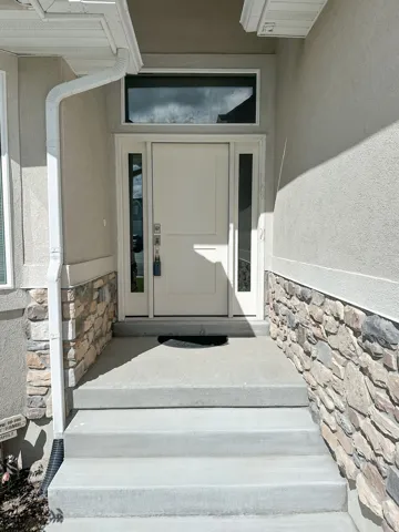 Inviting entry featuring a solid paneled door with glass side lites, a transom window, and stone veneer accents