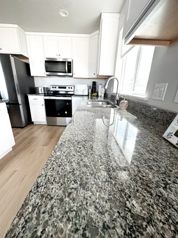 Granite countertops, white shaker-style cabinetry, stainless steel appliances, stainless steel sink with a gooseneck faucet, and wood-finish flooring