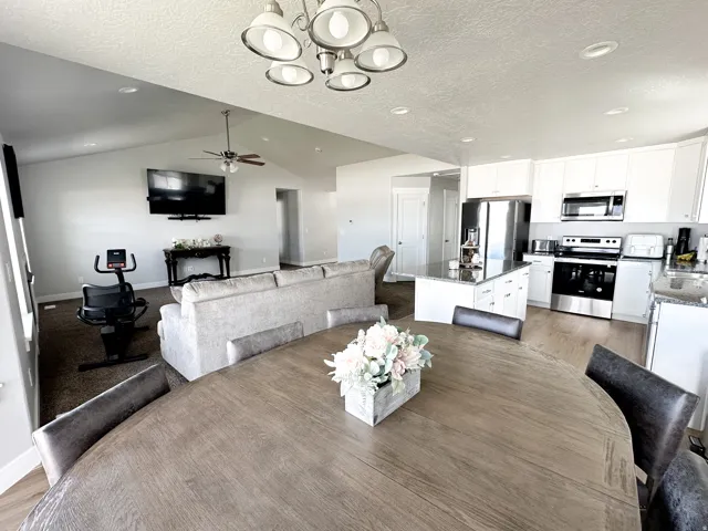 Vaulted ceilings with recessed lighting, wood-finish flooring, white cabinetry, stainless steel appliances, and a kitchen island with seating