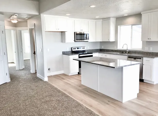 Kitchen featuring white cabinetry, granite-finish countertops, stainless steel appliances, a center island, and wood-finish flooring