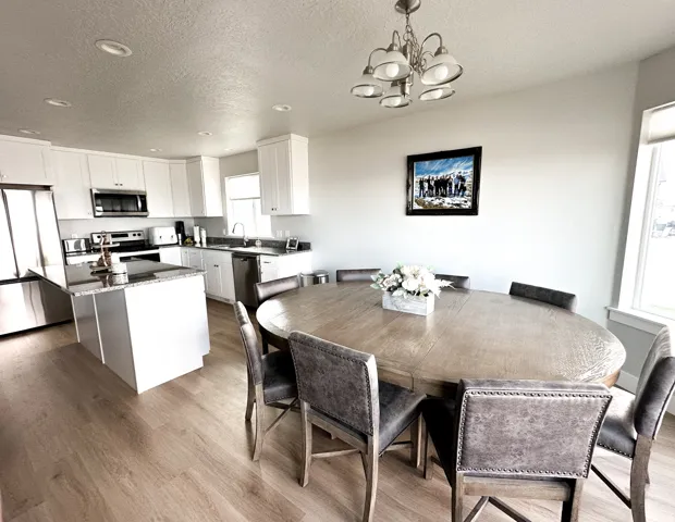 Kitchen and dining area featuring wood-finish flooring, white cabinetry, stainless steel appliances, and a kitchen island with a stone countertop