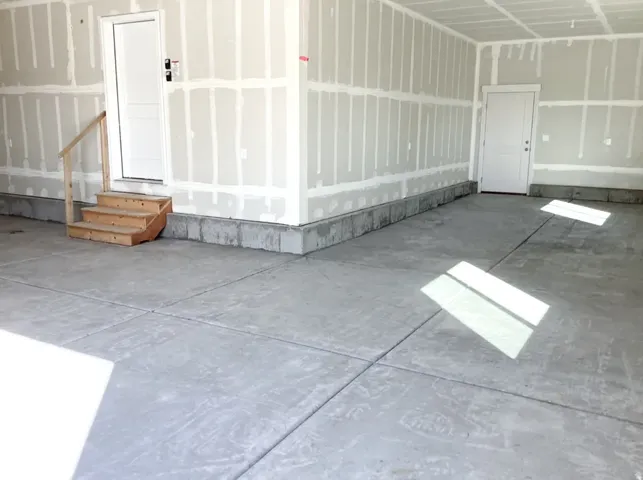 Unfinished garage space with concrete flooring, two white panel doors, and a wooden stair set with a handrail