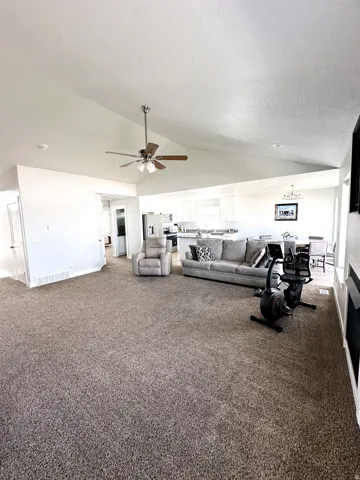Vaulted ceiling, ceiling fan with light fixture, neutral wall paint, carpeted flooring, and built-in fireplace