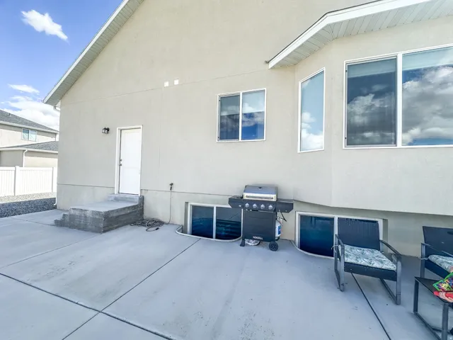 Concrete patio with a stucco exterior, multiple windows, and a white entry door