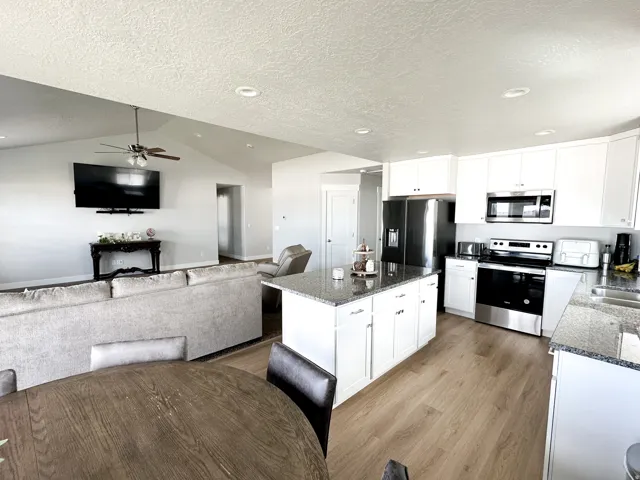 Kitchen featuring white cabinetry, stainless steel appliances, granite countertops, and wood-finish flooring