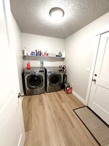 Laundry area with wood-finish flooring, overhead flush-mount lighting, and a wall-mounted shelf