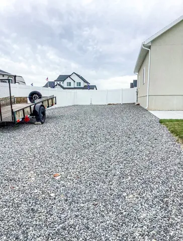 Expansive gravel area with white vinyl fencing and a stucco exterior
