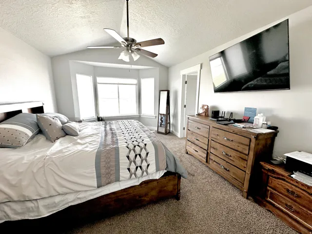 Carpeted room featuring a bay window, ceiling fan, and wall-mounted television