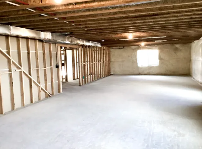 Expansive unfinished interior space featuring exposed wood joists, concrete flooring, framed interior walls, and a window opening