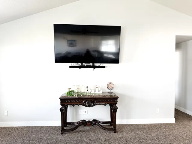 Vaulted ceiling with textured finish, wall-mounted television, and carpet flooring