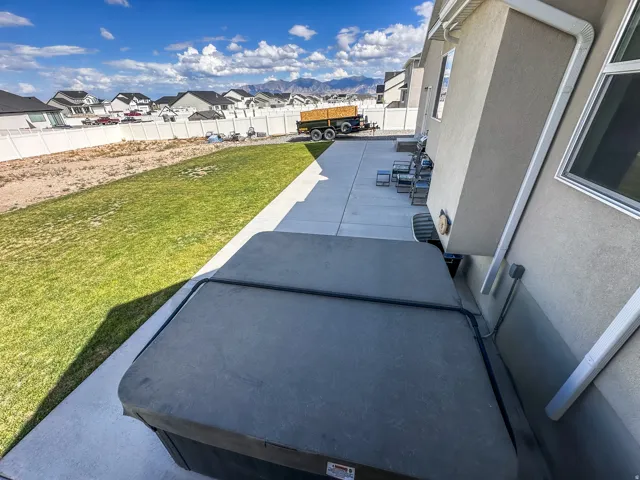 Expansive concrete patio with a spa, bordered by a manicured lawn and a white privacy fence