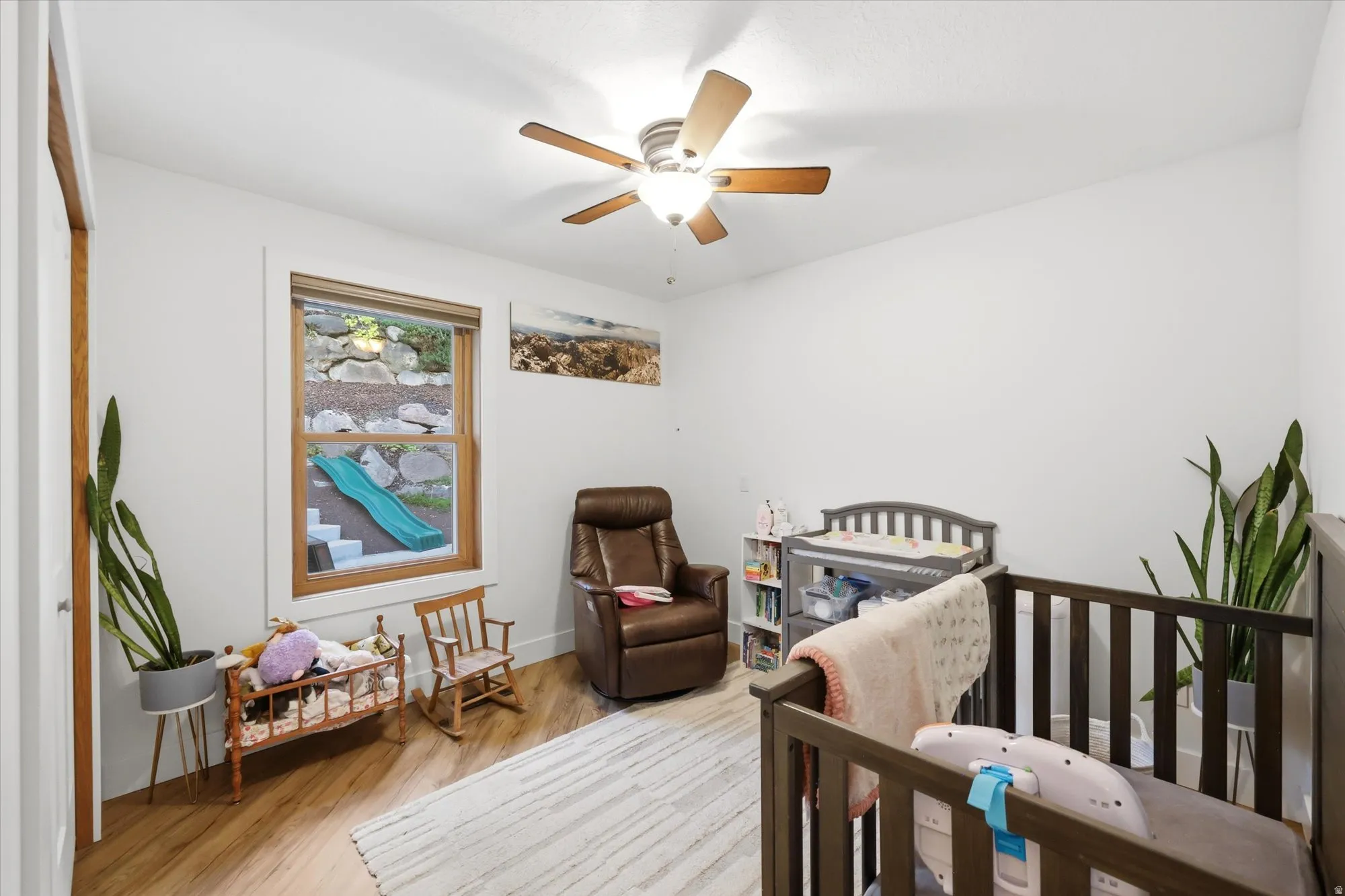 Bedroom with light wood-style flooring, a crib, and a ceiling fan