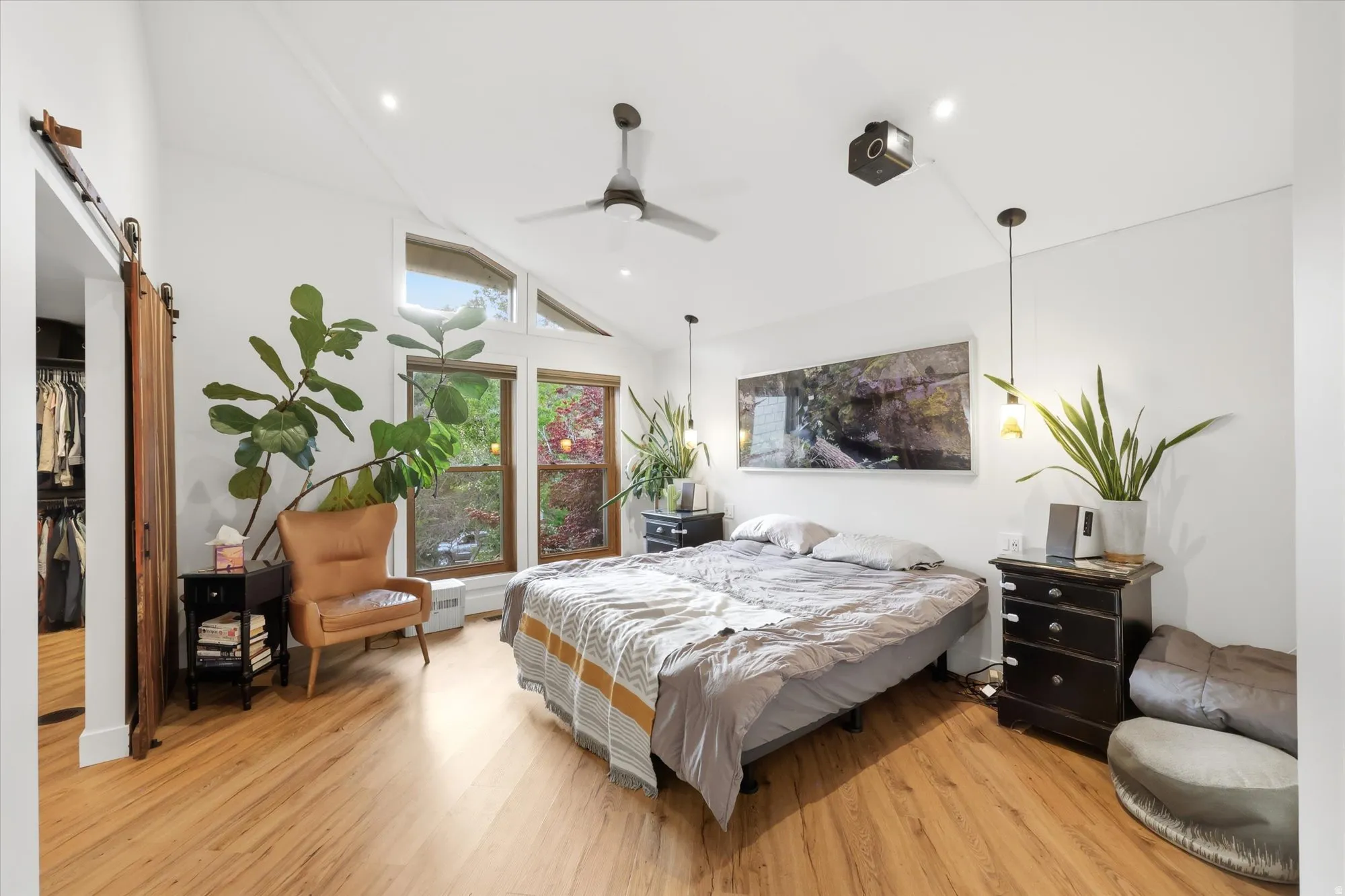 Bedroom with a barn door, light wood-style floors, and lofted ceiling