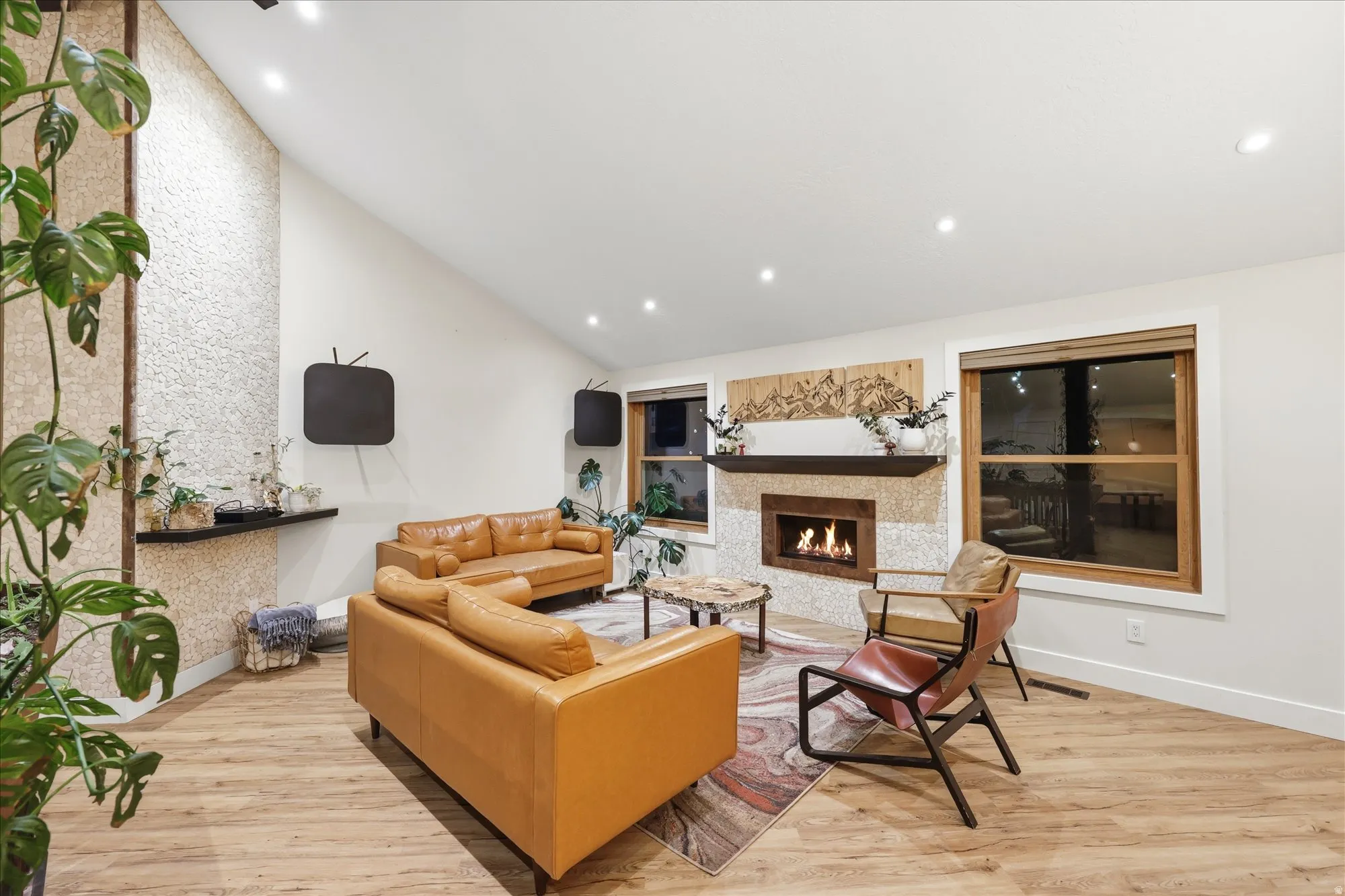 Living room featuring light wood finished floors, a warm lit fireplace, vaulted ceiling, and recessed lighting