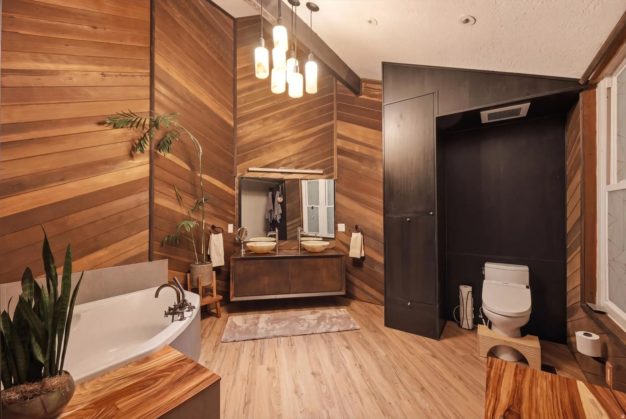 Bathroom featuring double vanity, a bath, light wood-style flooring, hanging lights, and vaulted ceiling