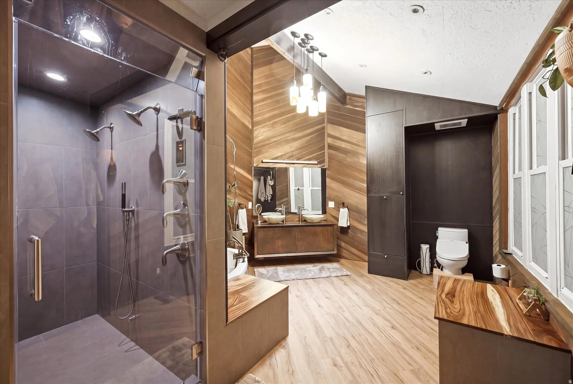 Full bathroom with vanity, light wood-type flooring, a stall shower, wood walls, and lofted ceiling