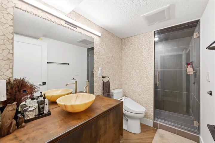 Full bath featuring a textured ceiling, vanity, a stall shower, wallpapered walls, and light wood-style floors