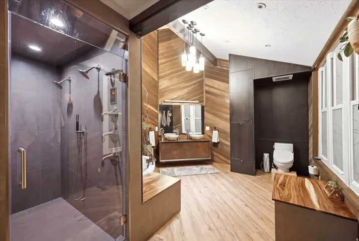 Full bathroom with vanity, light wood-type flooring, a stall shower, wood walls, and lofted ceiling
