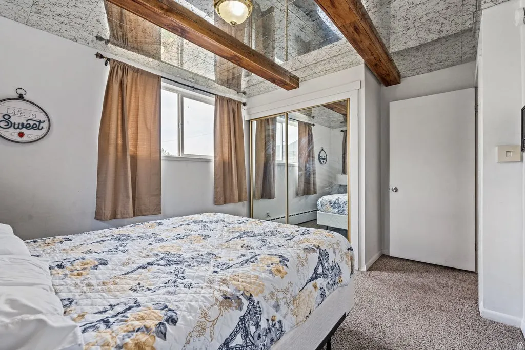 Bedroom featuring beam ceiling, light carpet, a closet, and baseboard heating
