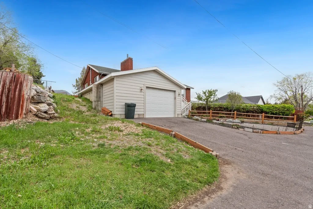 View of home's exterior with a chimney, asphalt driveway, an outbuilding, and an attached garage
