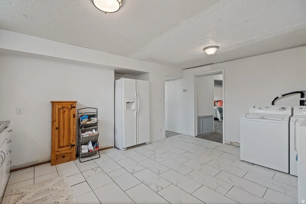 Laundry area with a textured ceiling, separate washer and dryer, and light marble finish flooring