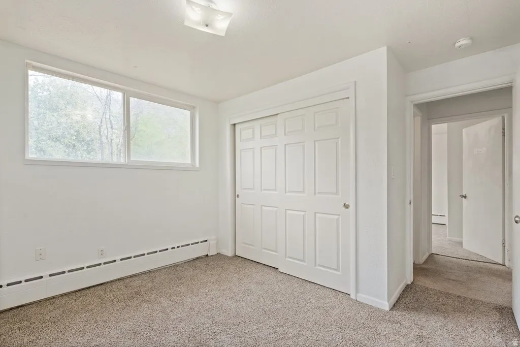Unfurnished bedroom with light carpet, baseboard heating, and a closet